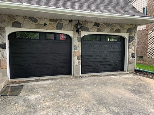 Deux portes de garage noires avec bordures blanches, côte à côte sur une maison en pierre.