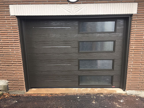 Porte de garage marron avec fenêtres, intégrée dans un cadre de maison typique.