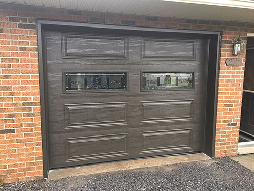 Garage avec une porte marron dotée de deux fenêtres, harmonisée avec le revêtement de la maison.