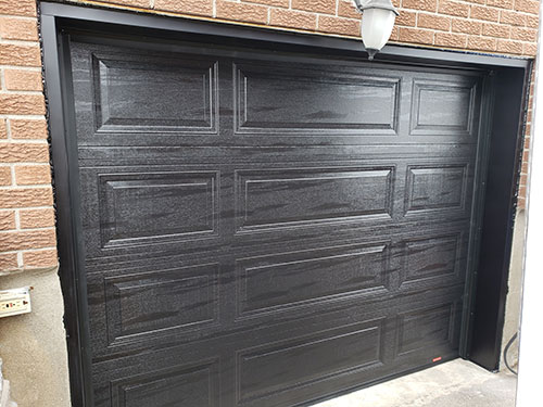 Porte de garage noire, éclairée par une lumière, mettant en valeur son design simple.