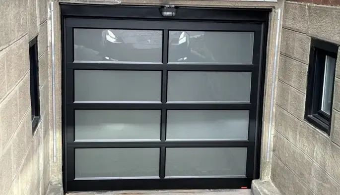 Une porte de garage moderne à panneaux de verre intégrée dans une entrée d'allée aux murs de brique et de béton.