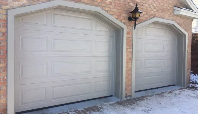 Deux portes de garage sable et une lumière au-dessus, sur une maison en brique rouge.